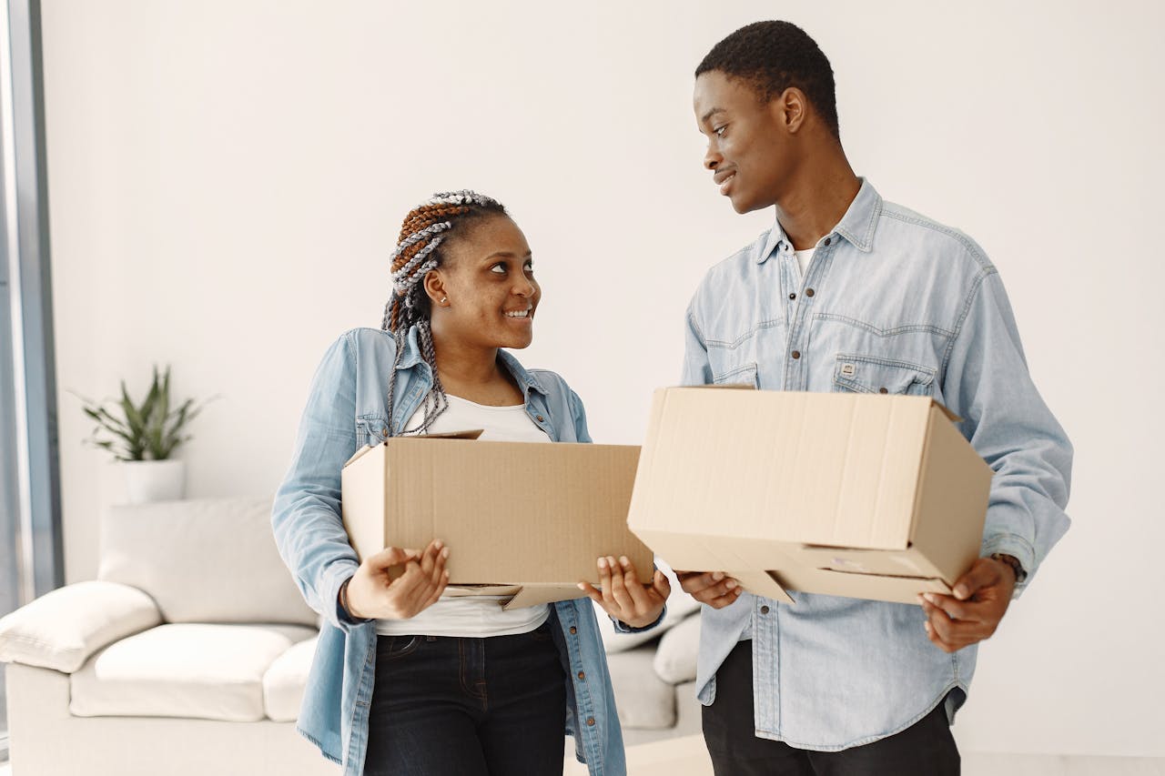 A joyful couple carrying cardboard boxes indoors during their move.