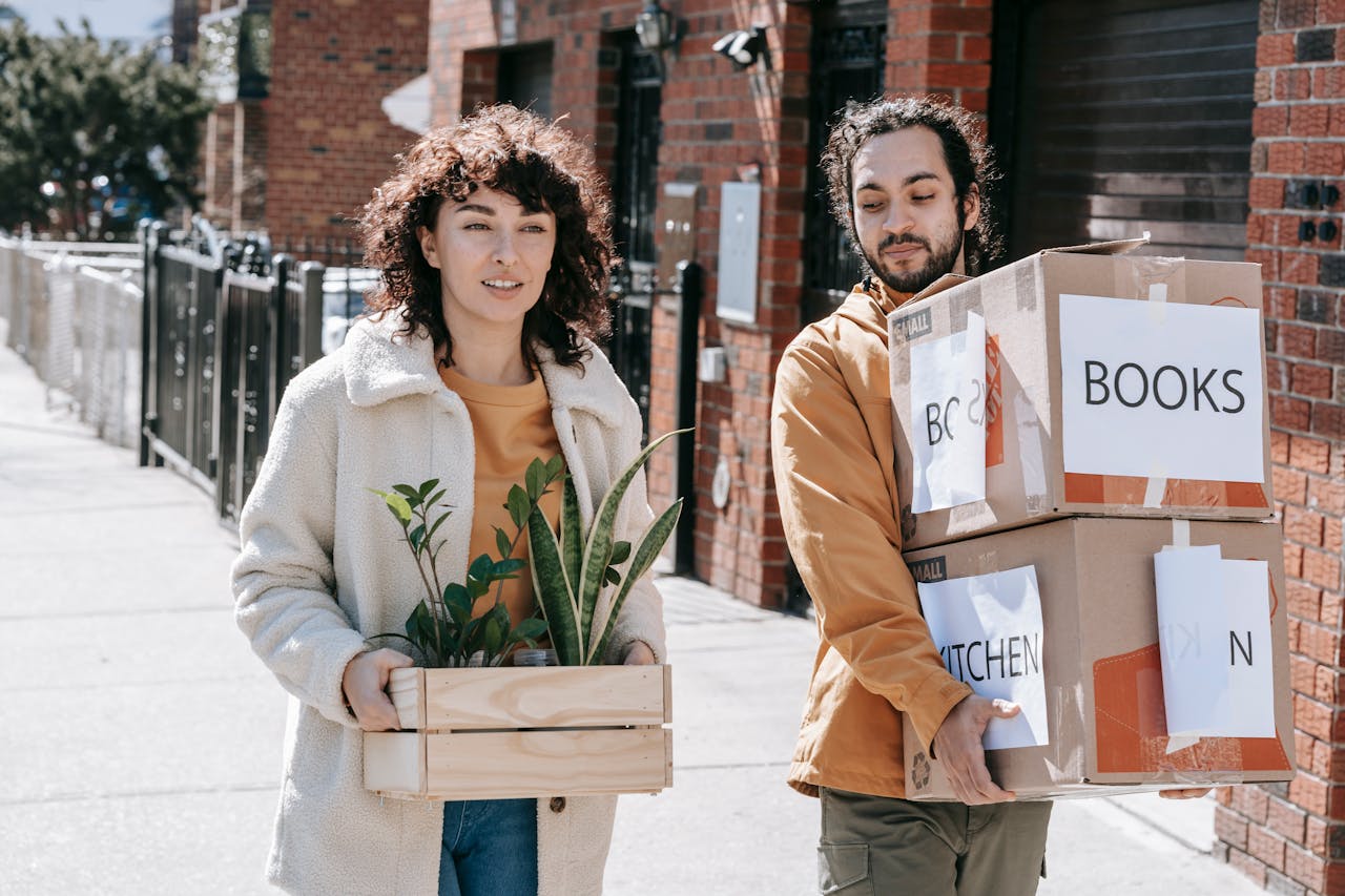 Young couple happily moving into their urban apartment with boxes and plants in daylight.