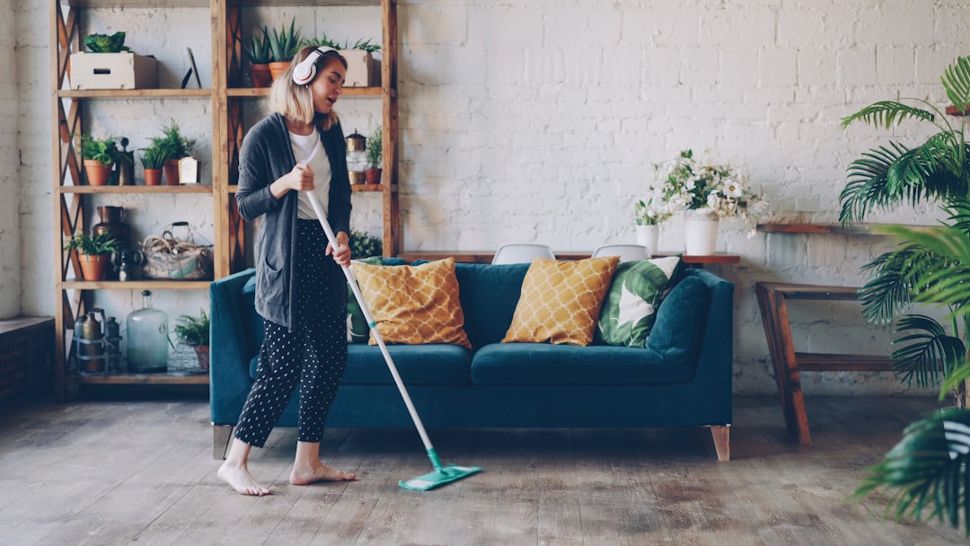Cheerful girl is mopping floor and listening to music with wireless headphones, she is singing and dancing enjoying rhythm cleaning her nice modern apartment. Joy and routine concept.